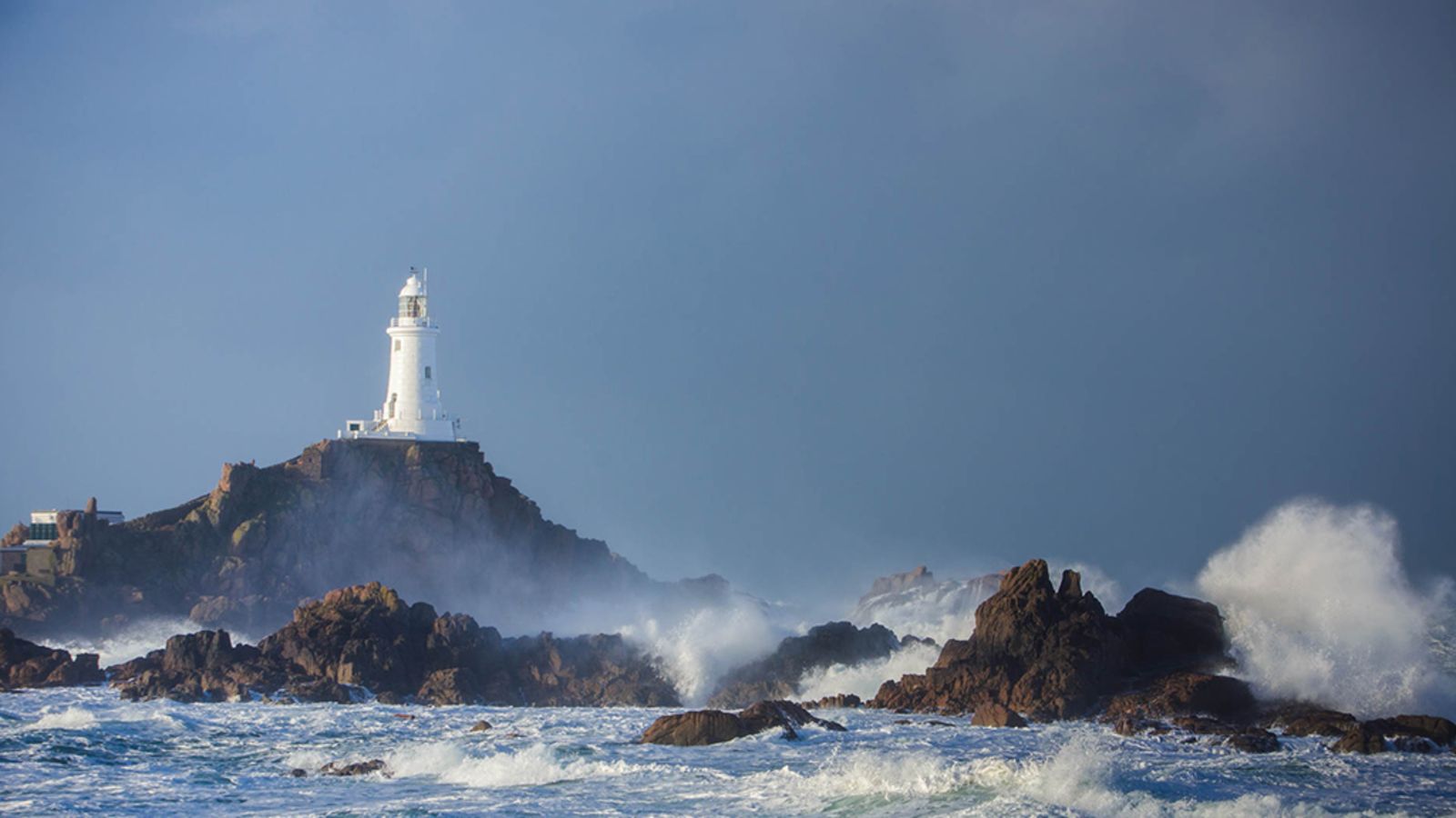 La Corbière Lighthouse above the rocky Jersey coastline, with Atlantic waves breaking below