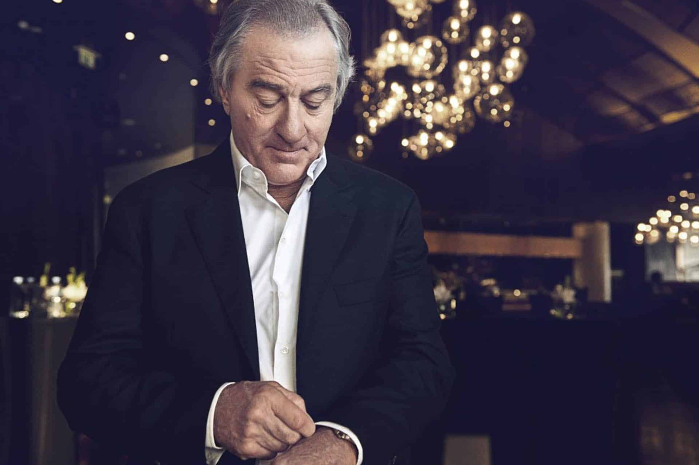 A man in a dark suit adjusting his watch, photographed by Oliver Doran